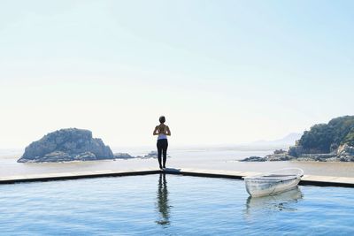 Rear view of woman exercising by swimming pool against sea