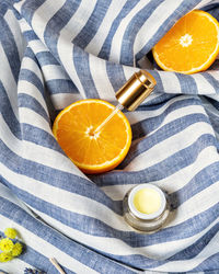 Orange halves with a cosmetic pipette and a jar of natural cream on striped textile background