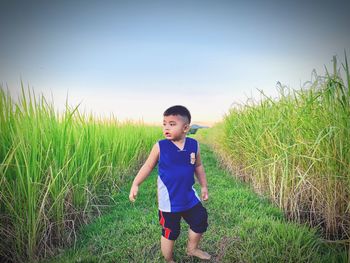 Boy looking away while standing on grass against sky