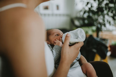 Midsection of woman feeding milk to newborn son at home