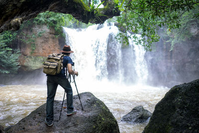 Rear view of man photographing waterfall in rainforest