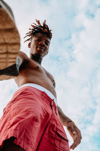 Low angle view of young man looking at camera against sky