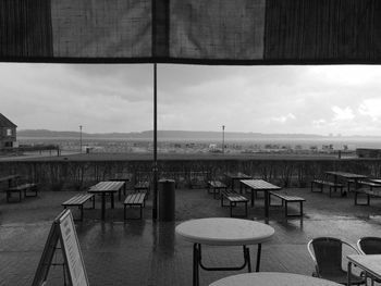 Empty chairs and table in cafe against sky