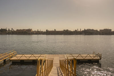 Pier over river by buildings against clear sky