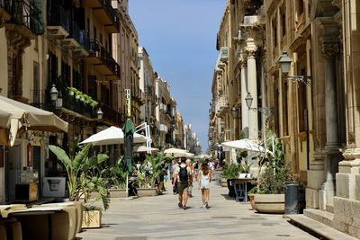 People walking on a walkable street with palm trees in sicily, italy