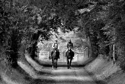 Rear view of people walking on road along trees