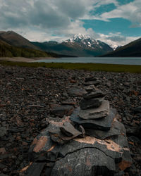 Rocks neatly stacked near icy blue glacier lake with mountain in background 