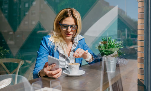 Young woman using mobile phone seen through glass at cafe