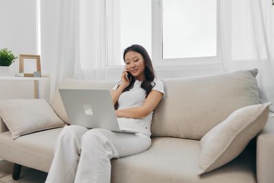 Young woman using laptop while sitting on sofa at home