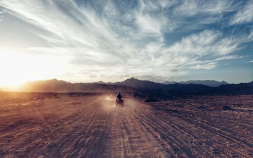 Rear view of person riding quadbike on desert against cloudy sky