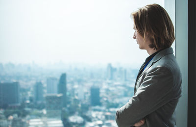 Side view of man looking at cityscape against sky