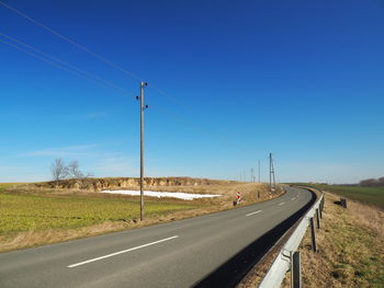 Road passing through land against clear blue sky