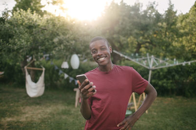 Portrait of smiling boy holding mobile phone while standing in backyard during garden party