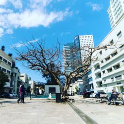 People on footpath by buildings in city against sky