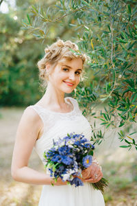 Portrait of bride holding bouquet standing against plants