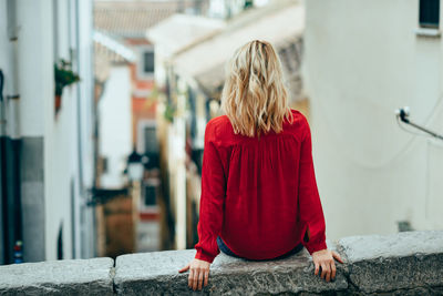 Rear view of young woman sitting on railing in city