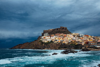 Buildings on rock formation by sea against cloudy sky