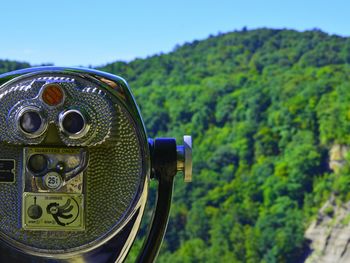 Close-up of coin-operated binoculars against trees