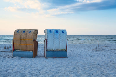 Hooded chairs on beach against sky