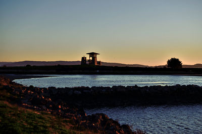 Silhouette lighthouse by sea against sky during sunset