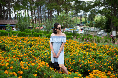 Smiling woman looking away while standing amidst flowering plants