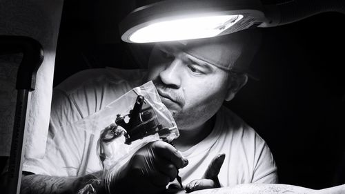 Close-up of artist looking at design on paper while making tattoo in darkroom