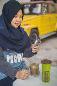 Smiling woman using mobile phone by drink on table