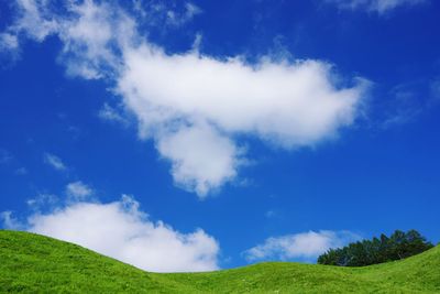 Low angle view of green hill against blue sky