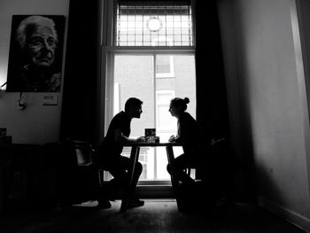 Side view of couple sitting on chairs by table against window at home