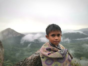 Portrait of cute boy standing in mountains against sky
