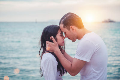 Young couple kissing against sea at sunset