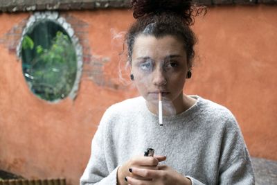 Young woman smoking while standing against wall