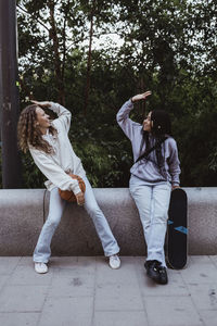 Female friends doing high-five while sitting on retaining wall at footpath