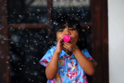 Portrait of girl blowing bubbles while standing in car