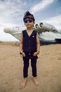 Rocker boy a child in black clothes stands against the abandoned plane on beach in summer