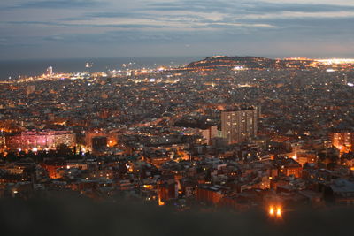 Aerial view of illuminated buildings in town against sky at night