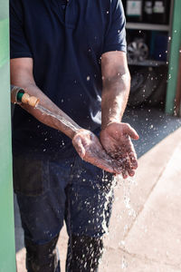 Crop anonymous male workman washing hands under tap with water after finishing work in repair service workshop