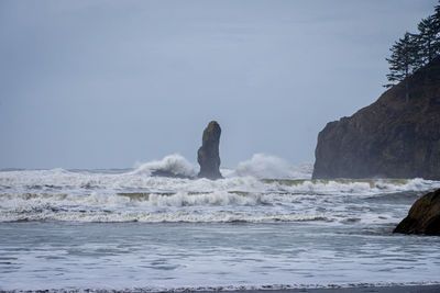 Sea waves splashing on rocks against sky