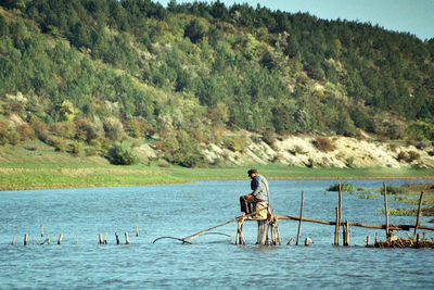 Young man with birds in river against trees