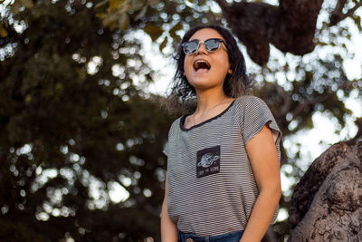 Young woman wearing sunglasses standing against trees