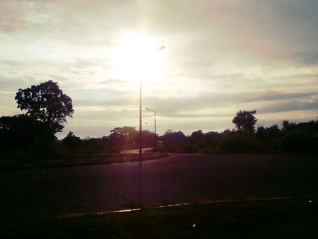 tree, sky, cloud - sky, sun, tranquility, tranquil scene, scenics, nature, beauty in nature, silhouette, sunset, sunlight, cloudy, landscape, field, cloud, sunbeam, grass, street light, road