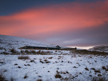 Snow covered field against sky during sunset