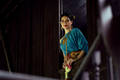 Women wearing thai national costumes standing by the window of a thai house