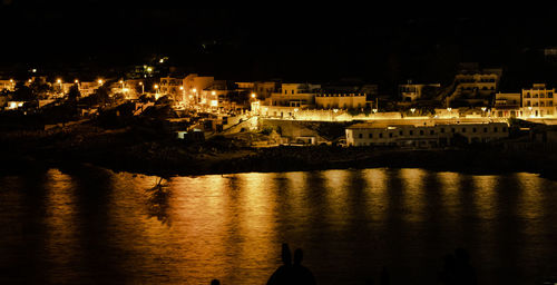 Illuminated buildings by sea against sky at night