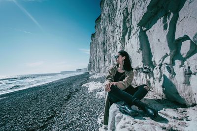 Young woman sitting on rock by sea against sky