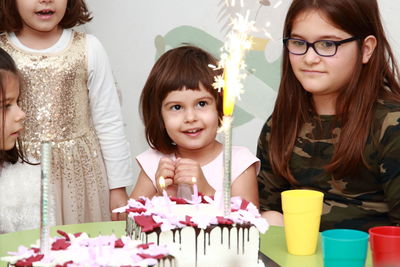 Four little girls at birthday party looking in the birthday cake with candles and fireworks