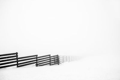 Wooden railing on snow covered land against clear sky