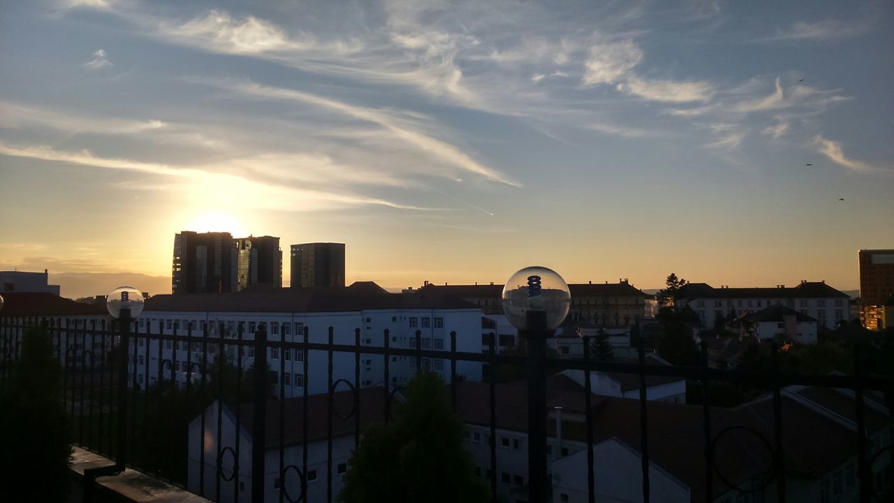 building exterior, sunset, architecture, built structure, sky, city, cityscape, cloud - sky, silhouette, building, residential building, residential structure, sunlight, cloud, orange color, outdoors, sun, residential district, city life, office building