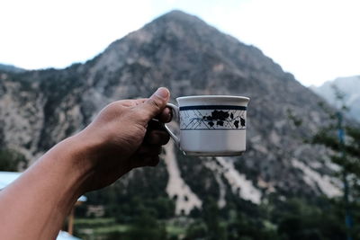 Midsection of person holding ice cream against mountains