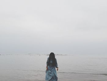 Rear view of woman standing at beach against sky